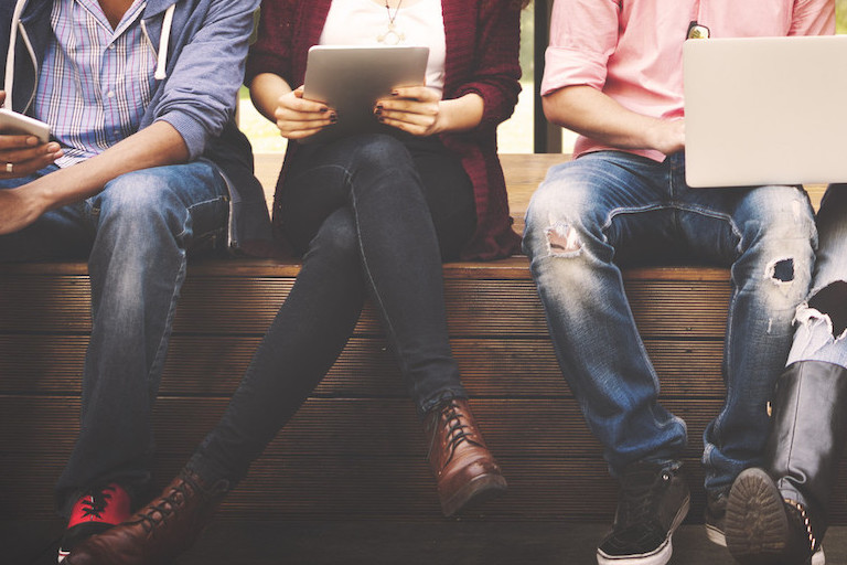 Foto: Junge Menschen sitzen nebeneinander und nutzen Handy sowie Laptops