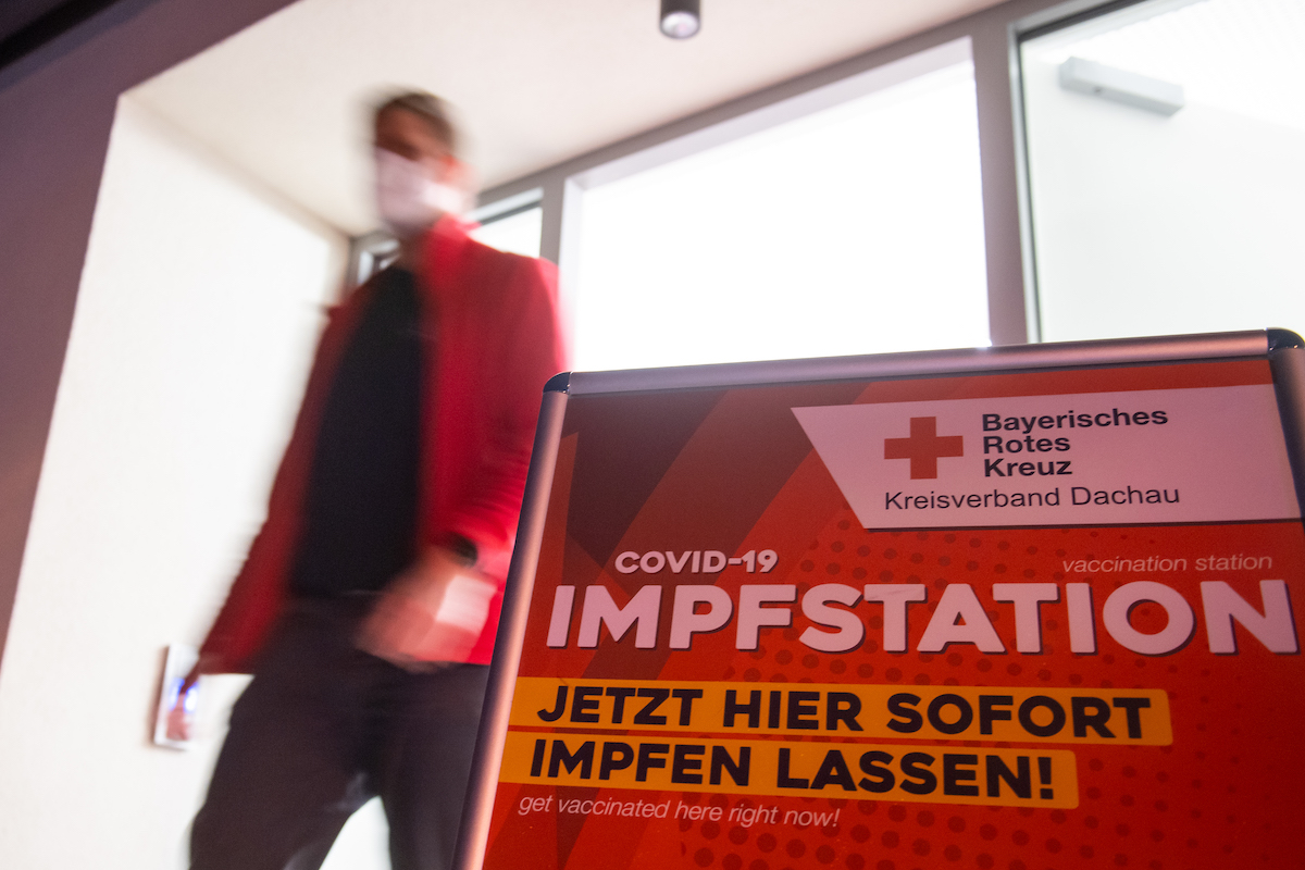 Foto: Ein Mann geht an einem Aufsteller mit der Aufschrift "Covid-19 Impftstation" vorbei. 