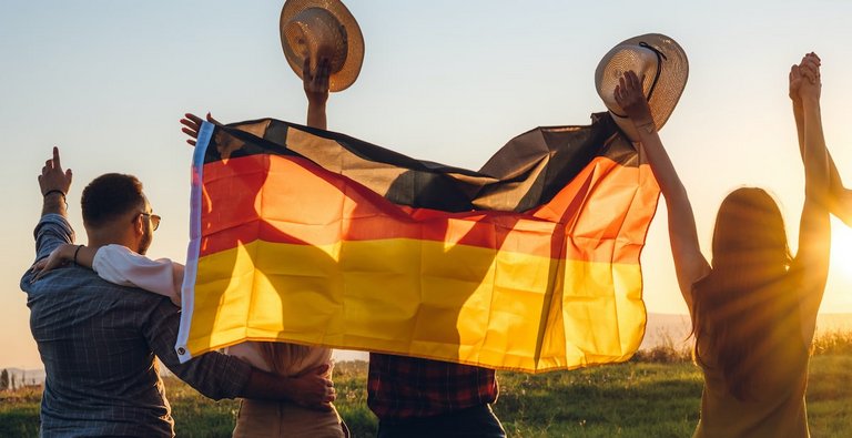 Foto: Junge Menschen mit Deutshcladnfahne jubeln bei Sonnenuntergang